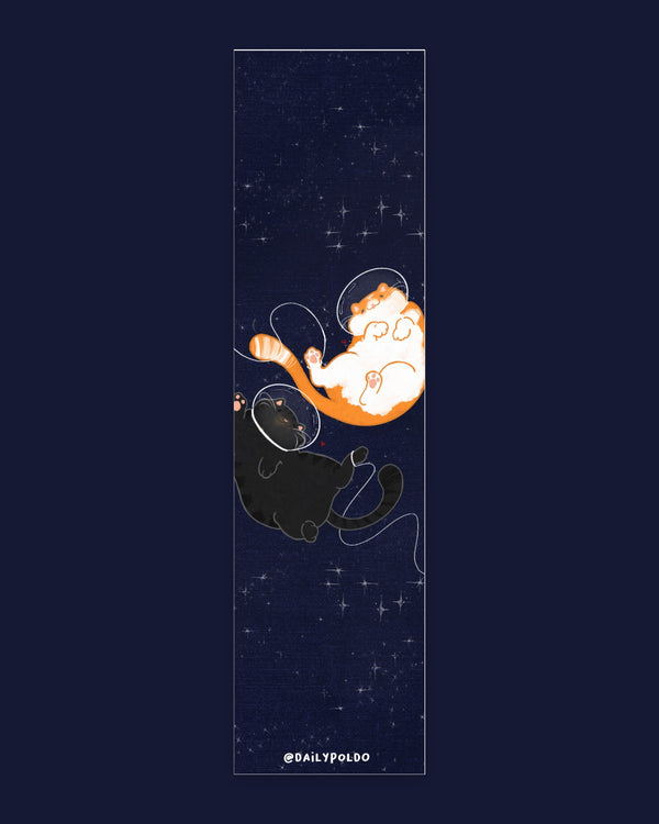 Due gatti paffuti, uno arancione e bianco e uno tigrato scuro, fluttuano con casco da astronauta su cielo blu pieno di stelle